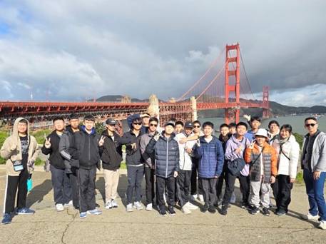 A group of people posing for a photo in front of a bridge Description automatically generated